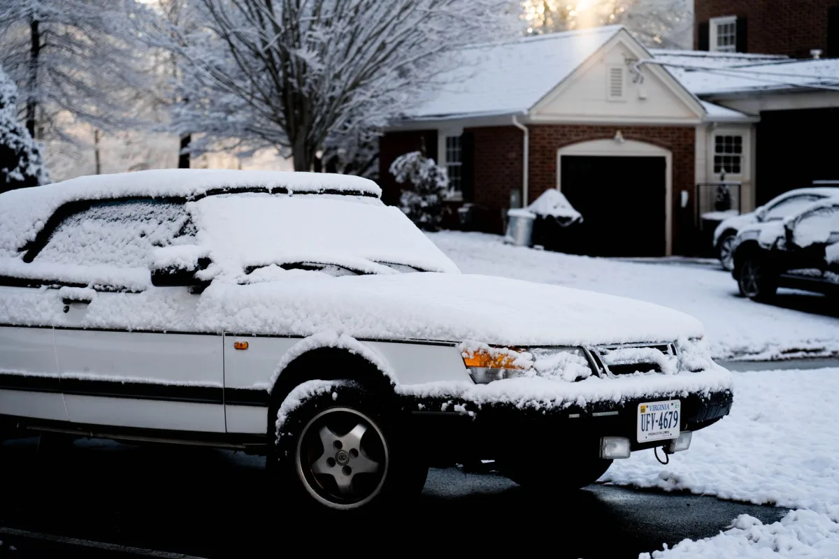 Snow-covered car parked on a residential driveway in front of a brick house