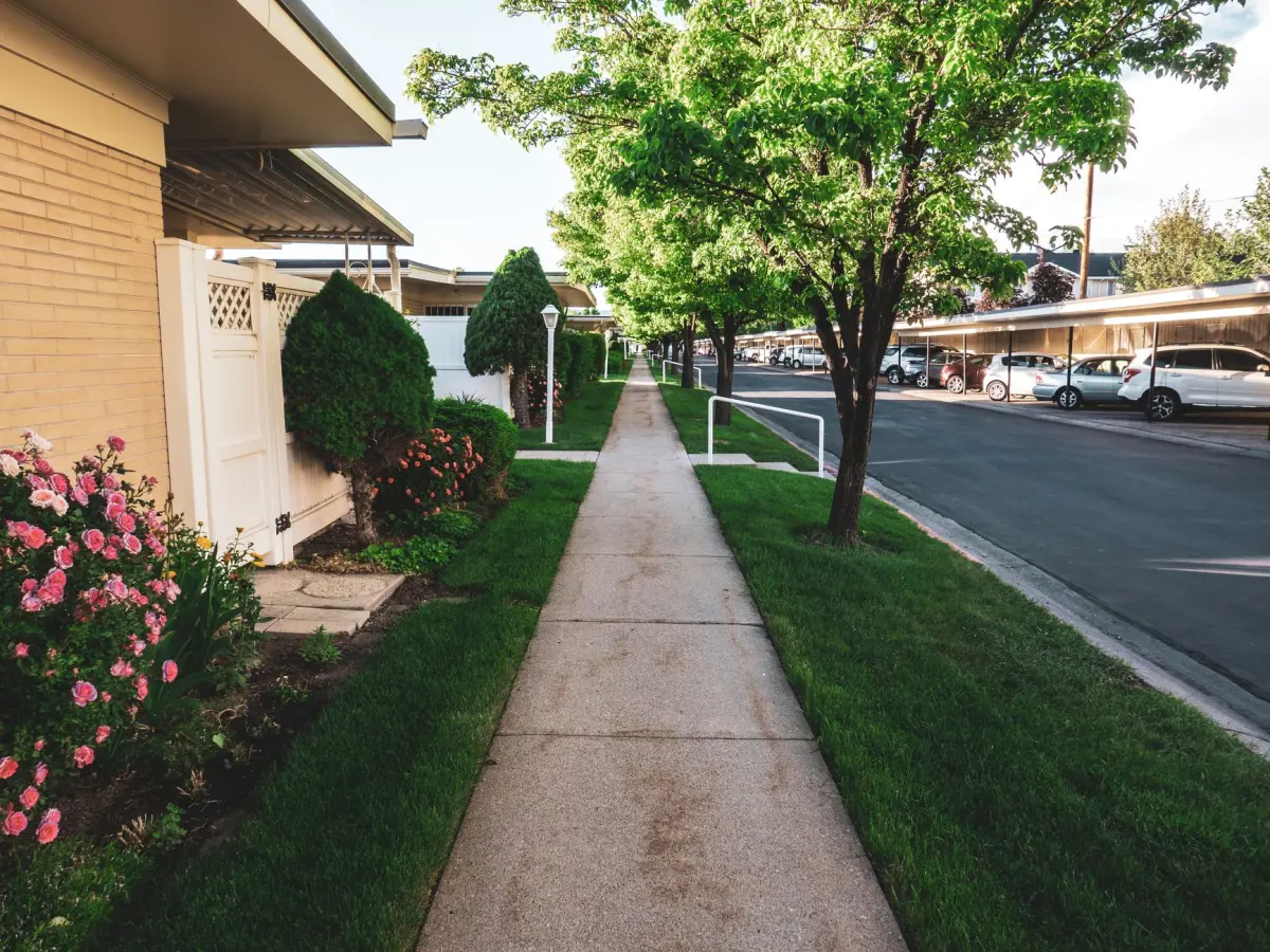 Concrete walkway running past single-storey homes with lawns and mature trees